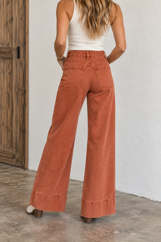 Back view of model wearing rust washed high-rise wide-leg jeans with patch pockets and wide hem detail.