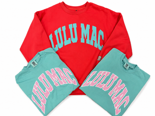 Bright coral red Lulu Mac crewneck sweatshirt featuring oversized turquoise arched lettering across the front and a small logo detail on the sleeve.