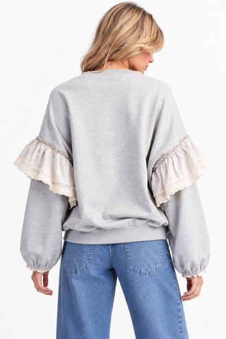Back view of a heather gray pullover with cream ruffle sleeve details, lace-trimmed cuffs, and a ribbed hem.