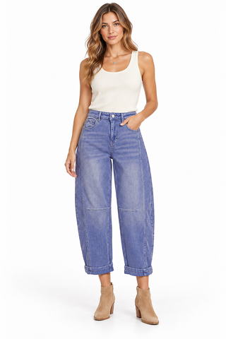 Front view of a model wearing faded Marlin blue barrel jeans with curved knee seams and rolled cuffs, styled with a cream tank and tan boots.