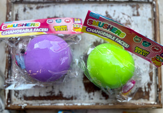 Purple Smushers squishy toy with interchangeable face pieces in clear packaging with a colorful “Changeable Faces” label.