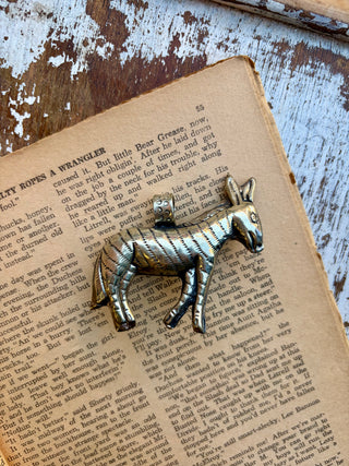  Antique-style silver donkey pendant featuring a turquoise stone accent, photographed on an open vintage book with a distressed wood background.