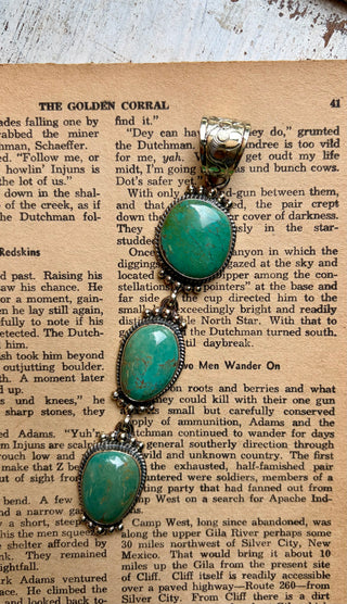 Three-stone turquoise drop pendant featuring graduated turquoise stones with natural matrix set in detailed antiqued alloy.