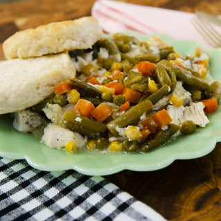 Crockstar Hearty Chicken Pot Pie with chicken, green beans, carrots, peas, and corn, served with biscuits on a light green plate.