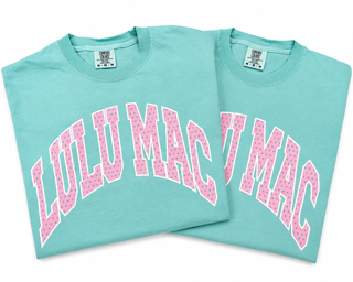 Two aqua Lulu Mac Comfort Colors T-shirts featuring oversized pink polka dot arched lettering with white outlines across the front.