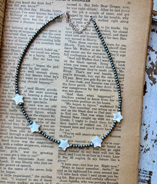 Sterling silver beaded necklace with five white freshwater pearl stars and an extender, displayed on an open vintage book.
