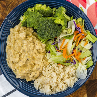 Crockstar Creamy Cajun Chicken served with white rice, broccoli, and a mixed green salad on a navy blue plate.