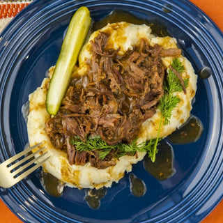 Crockstar Dill Pickle Pot Roast over mashed potatoes with gravy, a pickle spear, and fresh dill on a navy blue plate.