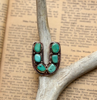 Horseshoe-shaped turquoise ring featuring six natural turquoise stones in an antiqued silver-tone setting with rope detailing.