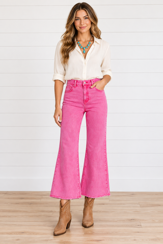 Model wearing hot pink high-rise wide-leg cropped jeans with raw hems, a cream blouse, turquoise necklace, and tan boots.