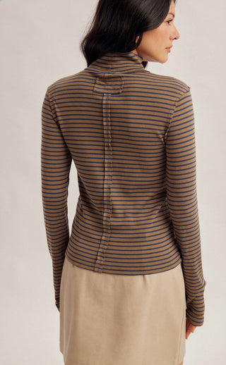 A woman shown from the back wearing a fitted long-sleeve top with thin horizontal brown and beige stripes, paired with a light beige skirt, against a plain light gray studio background.