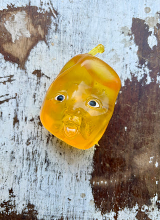 Translucent yellow Fruit Baby squishy with a molded baby face and small stem, displayed on distressed white wood.