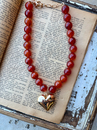 Amber-colored beaded necklace with a polished gold-tone heart pendant and extender chain, displayed on an open book.