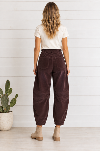 Back view of chocolate wine corduroy barrel pants showing rear patch pockets, belt loops, and knee seam detailing.