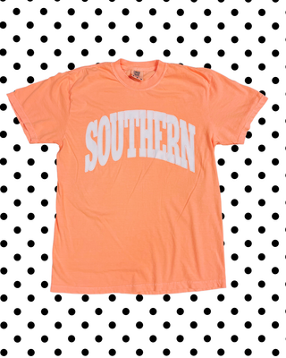 An orange short-sleeve t-shirt with 'SOUTHERN' printed in white arched block letters across the chest, displayed flat against a black and white polka dot background.