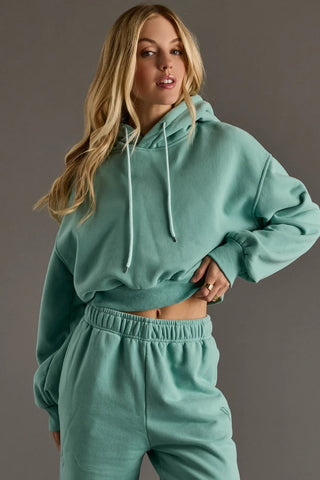 Woman wearing a teal hoodie and pants set against a gray background