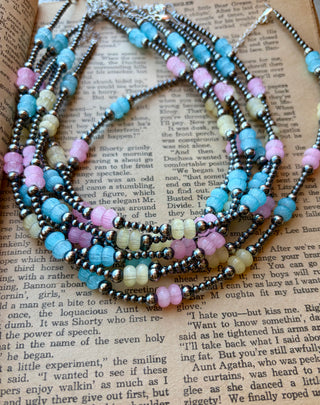Sterling silver pearl necklace with pastel blue, yellow, and pink glass beads, displayed on an open book.
