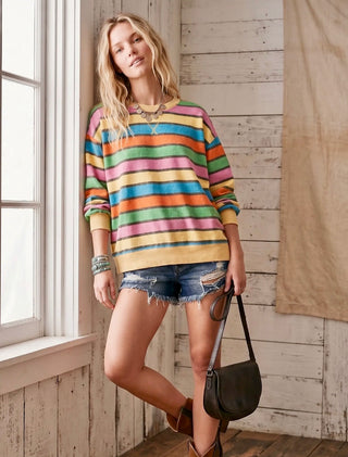 Woman wearing colorful striped sweatshirt with distressed denim shorts and boots