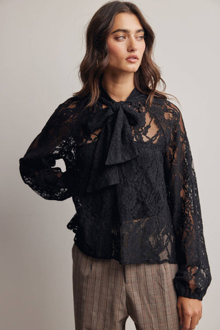 Woman wearing a black lace blouse with a bow tie against a plain background