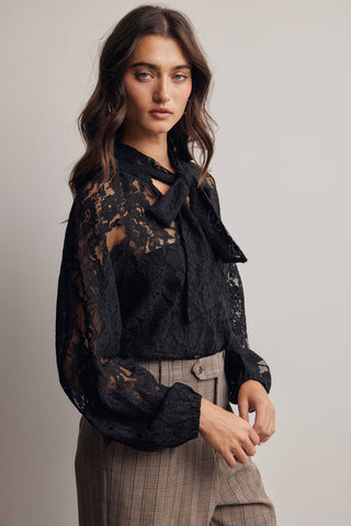 Woman wearing a black lace blouse with a bow and plaid pants on a neutral background